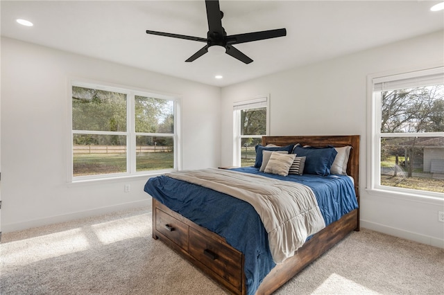 bedroom featuring ceiling fan, light colored carpet, and multiple windows