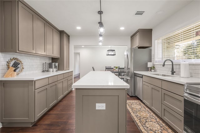 kitchen featuring stainless steel appliances, gray cabinetry, hanging light fixtures, a kitchen island, and sink