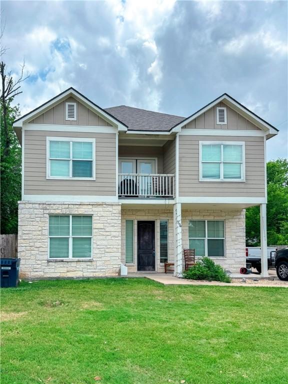 craftsman-style home with board and batten siding, a balcony, a front lawn, and stone siding