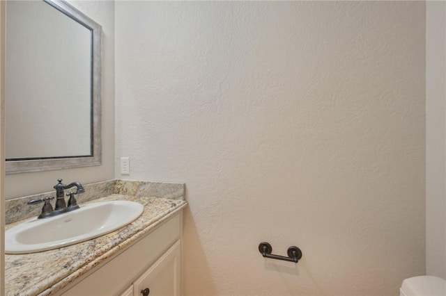 bathroom with toilet, a textured wall, and vanity