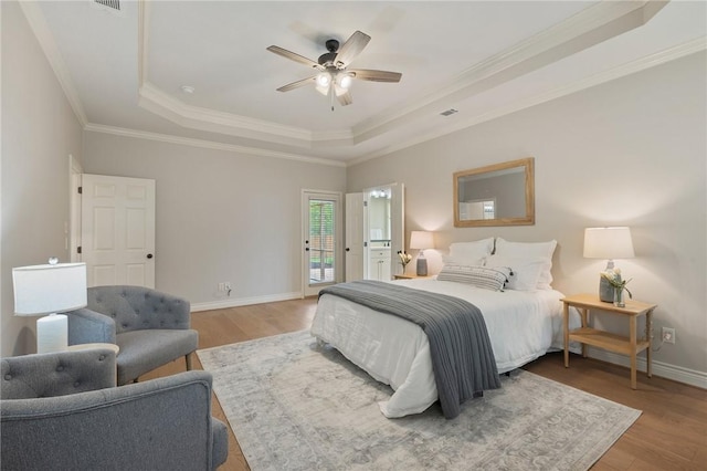 bedroom with crown molding, a tray ceiling, wood finished floors, and access to exterior