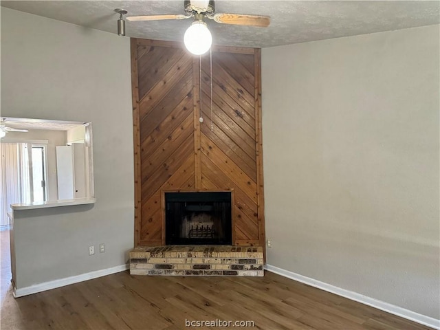 unfurnished living room featuring ceiling fan, a fireplace, dark wood-type flooring, and a textured ceiling