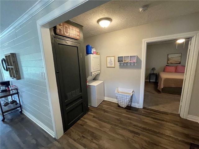 hallway featuring stacked washer / dryer, dark hardwood / wood-style flooring, and a textured ceiling