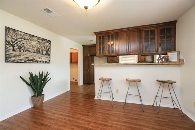 3000 Stevens Dr, Bryan, TX 77803 - kitchen featuring a kitchen bar, dark wood-type flooring, glass insert cabinets, and baseboards