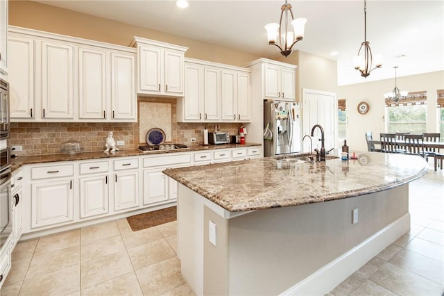 kitchen featuring light stone countertops, appliances with stainless steel finishes, sink, a center island with sink, and decorative light fixtures