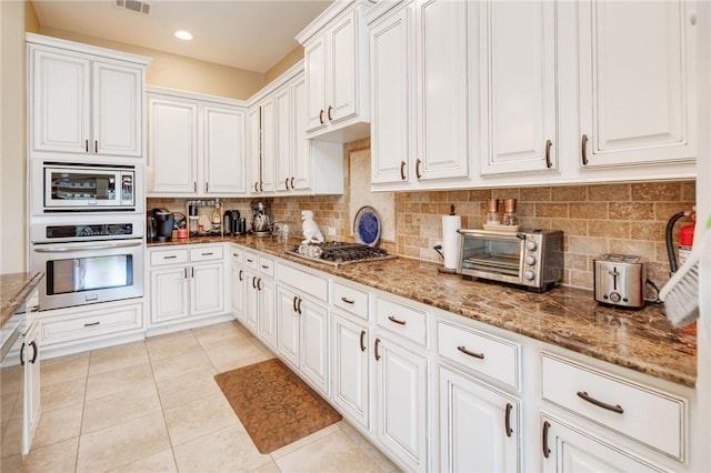 kitchen with light stone countertops, appliances with stainless steel finishes, tasteful backsplash, white cabinetry, and light tile patterned flooring