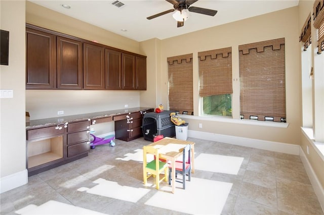 kitchen with light stone counters, dark brown cabinets, ceiling fan, and light tile patterned flooring