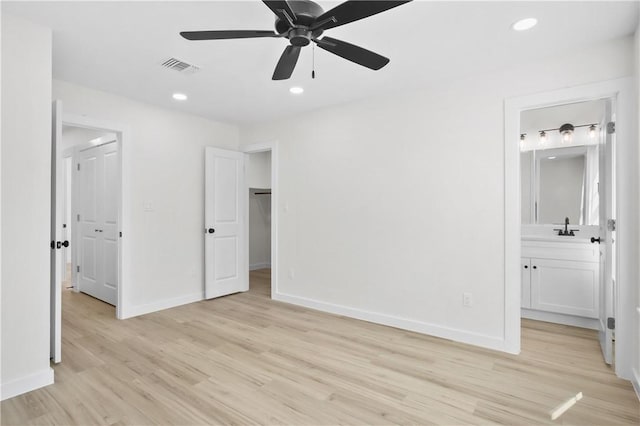 unfurnished bedroom with sink, ensuite bathroom, a walk in closet, and light hardwood / wood-style flooring