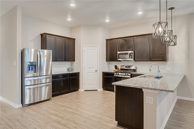 kitchen featuring sink, appliances with stainless steel finishes, light stone counters, dark brown cabinetry, and decorative light fixtures