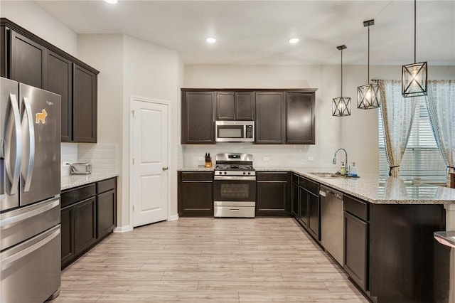 kitchen with appliances with stainless steel finishes, sink, hanging light fixtures, light hardwood / wood-style floors, and kitchen peninsula