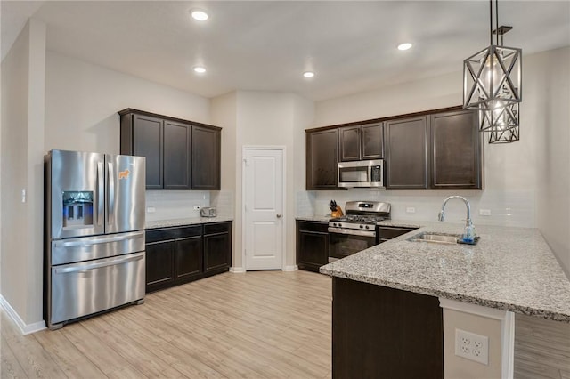 kitchen featuring appliances with stainless steel finishes, pendant lighting, sink, decorative backsplash, and light hardwood / wood-style flooring