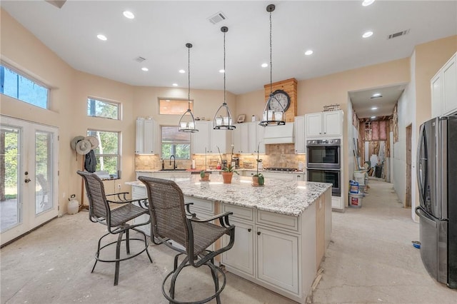 kitchen with multiple ovens, decorative light fixtures, stainless steel refrigerator, white cabinets, and a center island