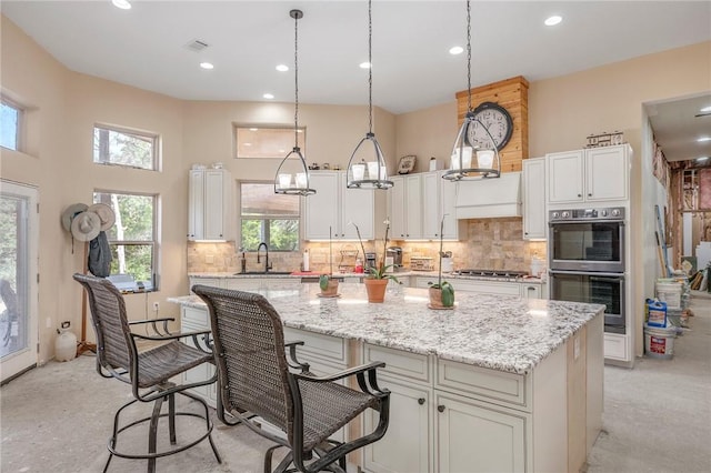 kitchen with stainless steel appliances, a kitchen breakfast bar, hanging light fixtures, a kitchen island with sink, and light stone counters