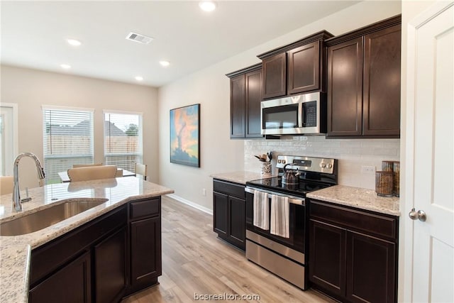 kitchen featuring light wood-type flooring, light stone counters, dark brown cabinetry, stainless steel appliances, and sink