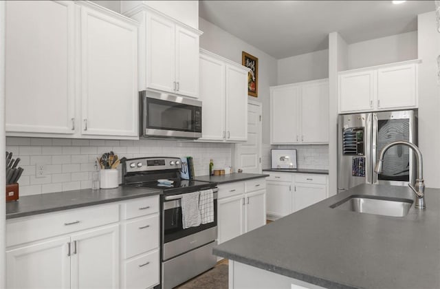 kitchen with appliances with stainless steel finishes, dark countertops, a sink, white cabinetry, and backsplash
