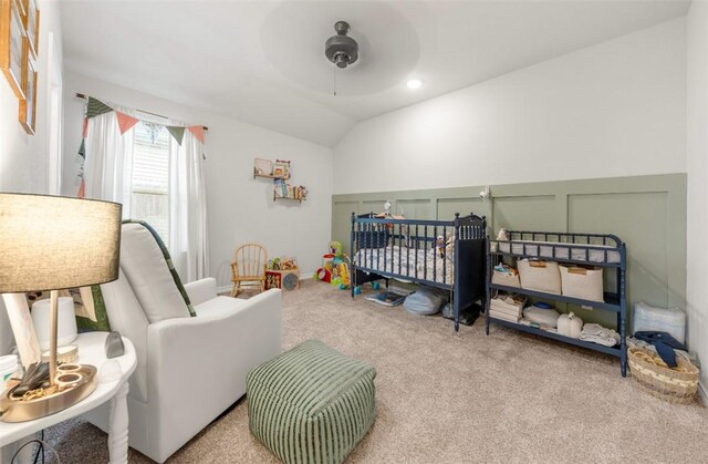 bedroom featuring carpet flooring, a decorative wall, vaulted ceiling, a nursery area, and a wainscoted wall