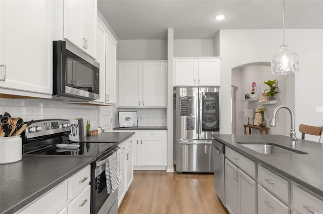 kitchen featuring stainless steel appliances, a sink, dark countertops, decorative backsplash, and white cabinets