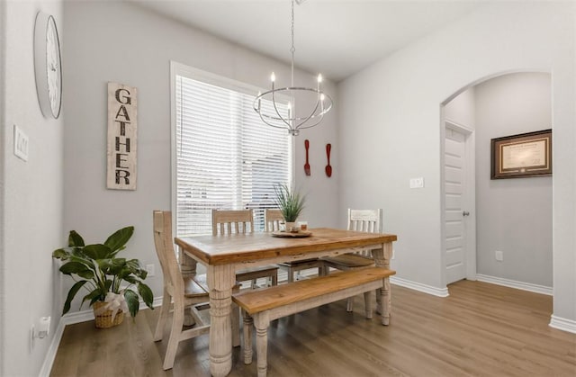 dining room with arched walkways, light wood-style floors, baseboards, and a chandelier