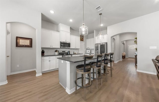 kitchen featuring stainless steel appliances, arched walkways, dark countertops, a kitchen breakfast bar, and white cabinetry