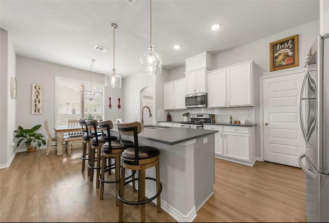 kitchen with appliances with stainless steel finishes, a sink, light wood-type flooring, dark countertops, and tasteful backsplash