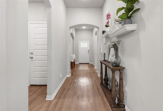 doorway to outside featuring arched walkways, wood finished floors, and baseboards