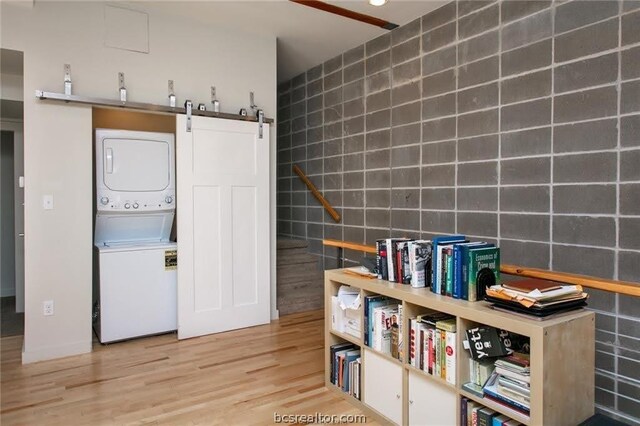 clothes washing area with a barn door, light hardwood / wood-style floors, stacked washer / dryer, and tile walls