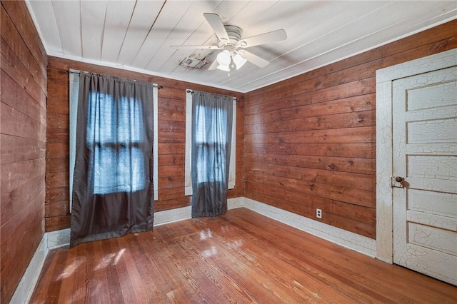 empty room featuring baseboards, hardwood / wood-style flooring, wood walls, and ceiling fan