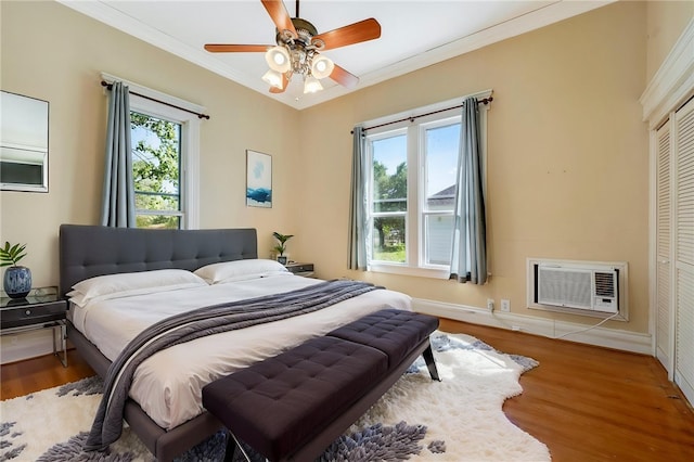 bedroom featuring wood finished floors, a closet, baseboards, ornamental molding, and a wall unit AC