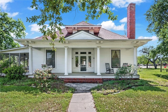 back of property with a porch, a lawn, a shingled roof, and a chimney