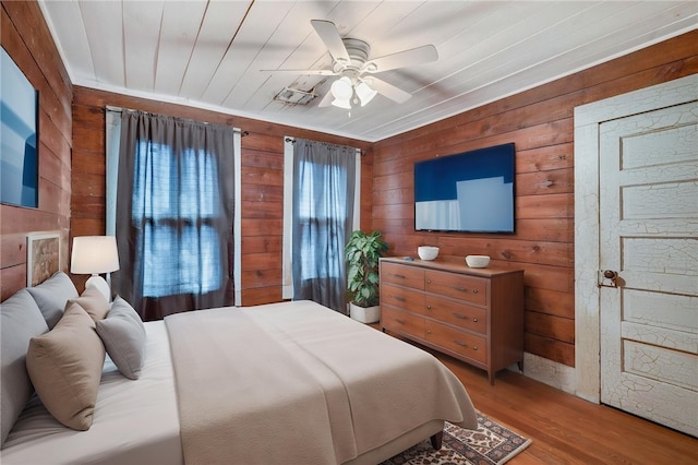 bedroom featuring wood walls, a ceiling fan, and light wood-type flooring