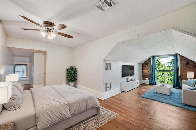 bedroom featuring wood walls, vaulted ceiling, visible vents, baseboards, and light wood-style flooring