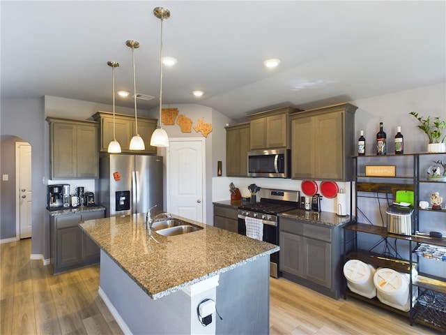 kitchen with hanging light fixtures, sink, dark stone countertops, appliances with stainless steel finishes, and light hardwood / wood-style floors