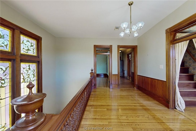 corridor with a notable chandelier, light hardwood / wood-style floors, and wooden walls