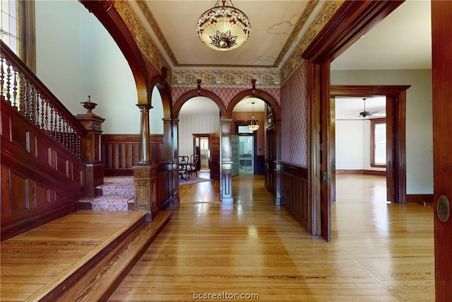 hall with ornate columns, light hardwood / wood-style floors, and ornamental molding