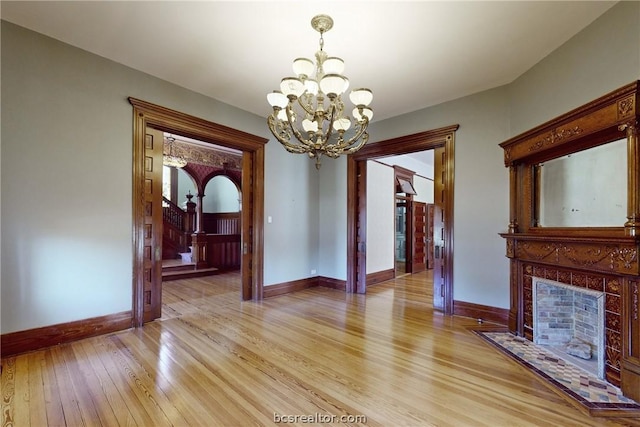 unfurnished dining area featuring a chandelier, light wood-type flooring, and a tiled fireplace