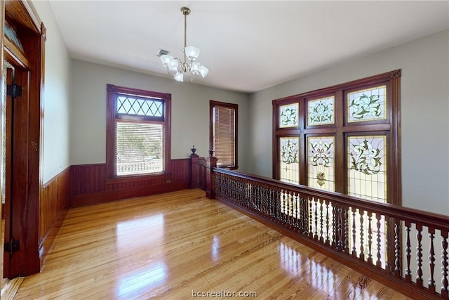 empty room with a chandelier, light hardwood / wood-style flooring, and wood walls