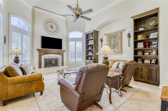 living room with crown molding, a fireplace with raised hearth, light tile patterned floors, and a ceiling fan