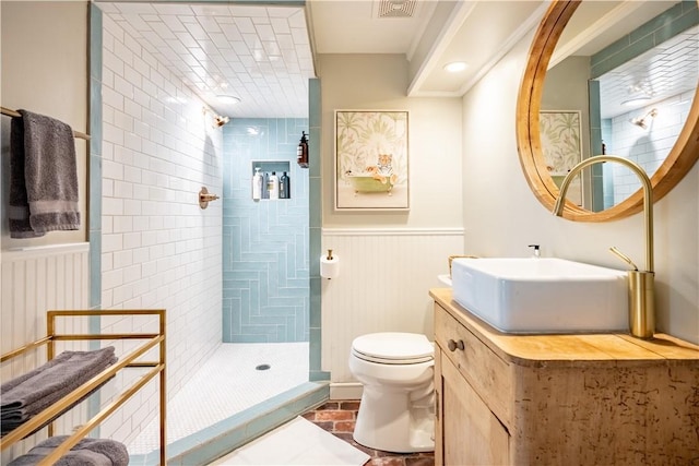 bathroom with toilet, a tile shower, and vanity