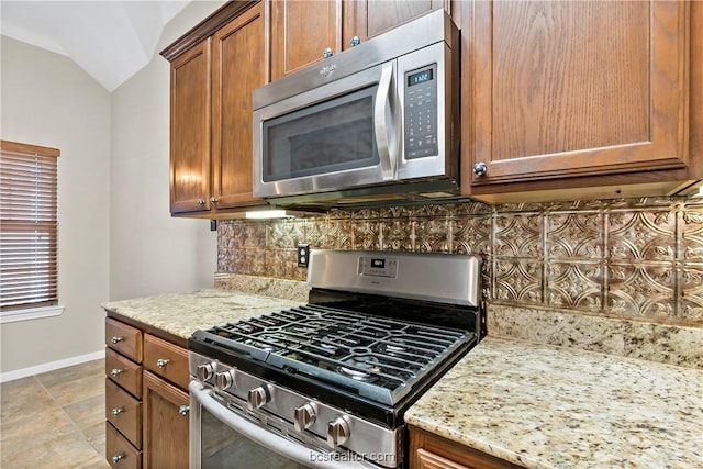 kitchen featuring decorative backsplash, light stone countertops, lofted ceiling, and stainless steel appliances