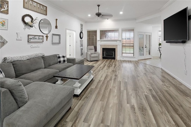 living room featuring a fireplace, french doors, light hardwood / wood-style flooring, ceiling fan, and crown molding