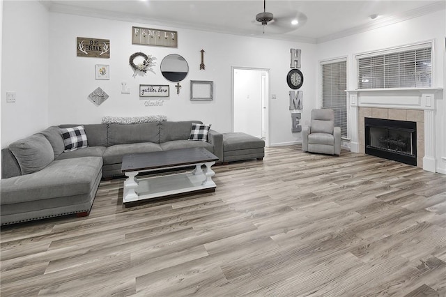 living room featuring light hardwood / wood-style flooring, crown molding, and a tiled fireplace