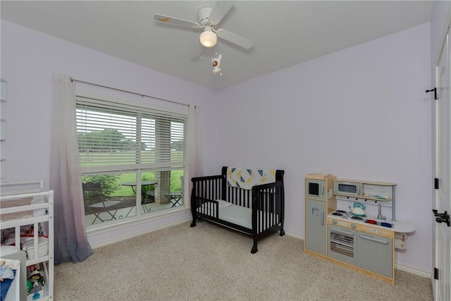 bedroom with a nursery area, baseboards, ceiling fan, and carpet