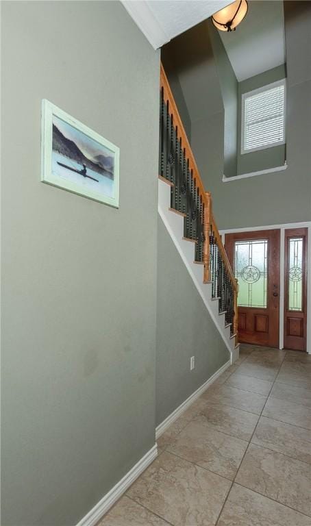 entryway featuring light tile patterned floors, a high ceiling, stairs, and baseboards