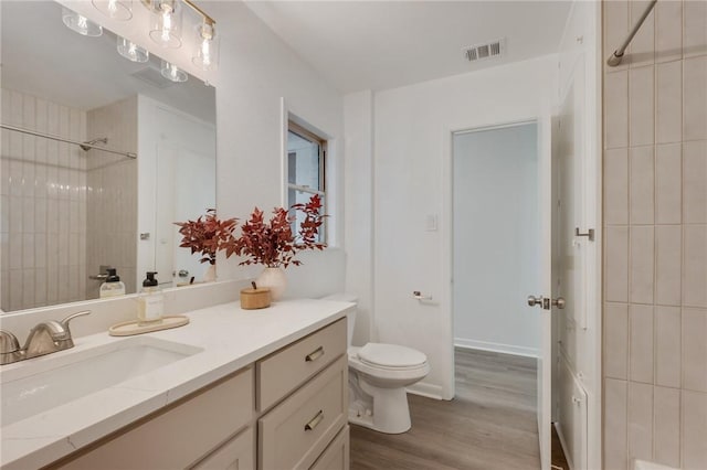 bathroom featuring wood finished floors, walk in shower, toilet, vanity, and visible vents