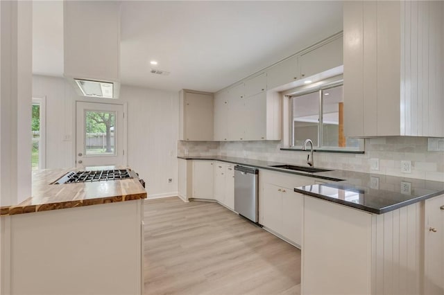 kitchen with a sink, stainless steel appliances, light wood-style floors, tasteful backsplash, and wooden counters
