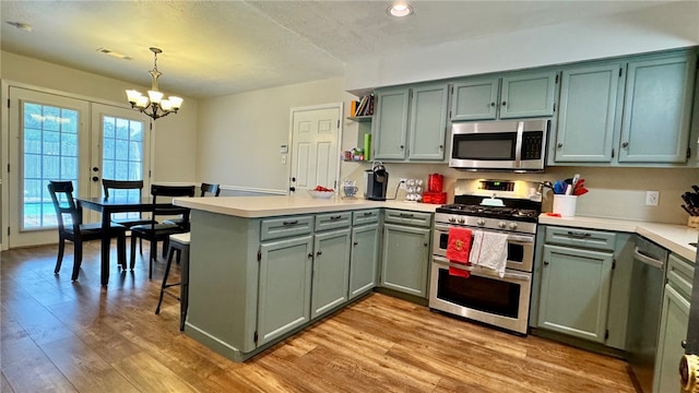 kitchen featuring an inviting chandelier, decorative light fixtures, light wood-type flooring, kitchen peninsula, and stainless steel appliances