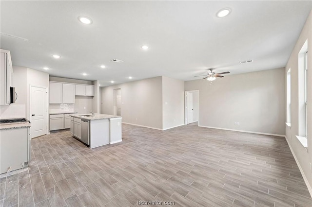 kitchen featuring light wood-type flooring, ceiling fan, a kitchen island with sink, sink, and white cabinets