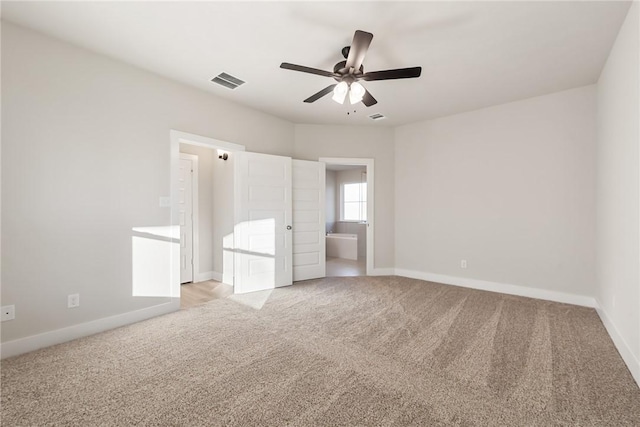 unfurnished bedroom featuring ceiling fan, light colored carpet, and ensuite bath