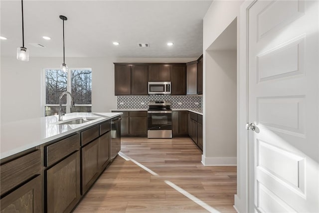 kitchen featuring dark brown cabinets, stainless steel appliances, sink, light hardwood / wood-style floors, and hanging light fixtures