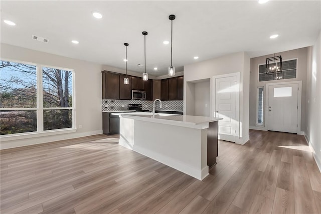 kitchen featuring backsplash, a kitchen island with sink, hanging light fixtures, light hardwood / wood-style flooring, and dark brown cabinets